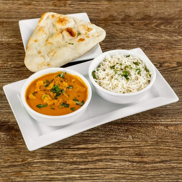 Chicken curry with rice and naan bread on a white rectangular plate, on a wooden table.