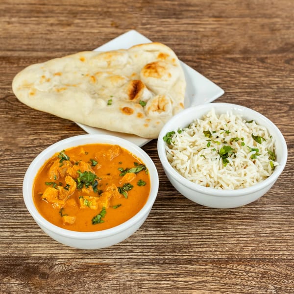 Chicken curry, rice, and naan bread are presented on a rustic wooden table.