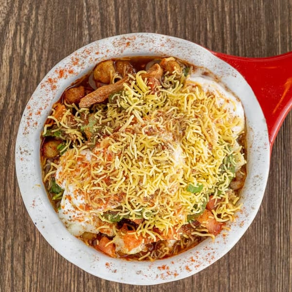 A close-up, top-down view of a colorful Indian chaat dish in a white and red bowl.