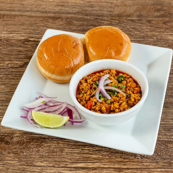 Keema Pav, a bowl of minced meat curry with two buns, sliced red onions, and a lime wedge.