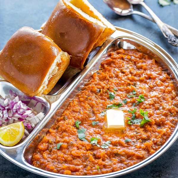Pav Bhaji, a vibrant Indian street food, served with buttered pav, chopped onions, and lemon.
